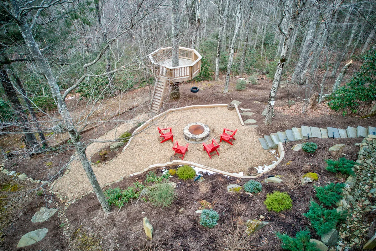 This image captures an inviting outdoor fire pit area with a circle of red chairs and a raised deck in the background, all set amidst lush greenery. The open space and natural surroundings are perfect for both relaxation and play, reinforcing the idea of a pet-friendly, outdoor-centric getaway.