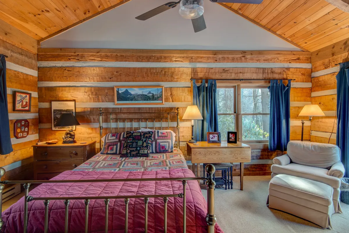 A warmly lit master suite featuring a plush bed with soft linens, a window letting in natural light, a nightstand, and a comfortable armchair positioned for relaxed reading or enjoying a morning coffee. The inviting atmosphere is enhanced by simple decor and thoughtful placement of furniture, creating a private and restful escape.