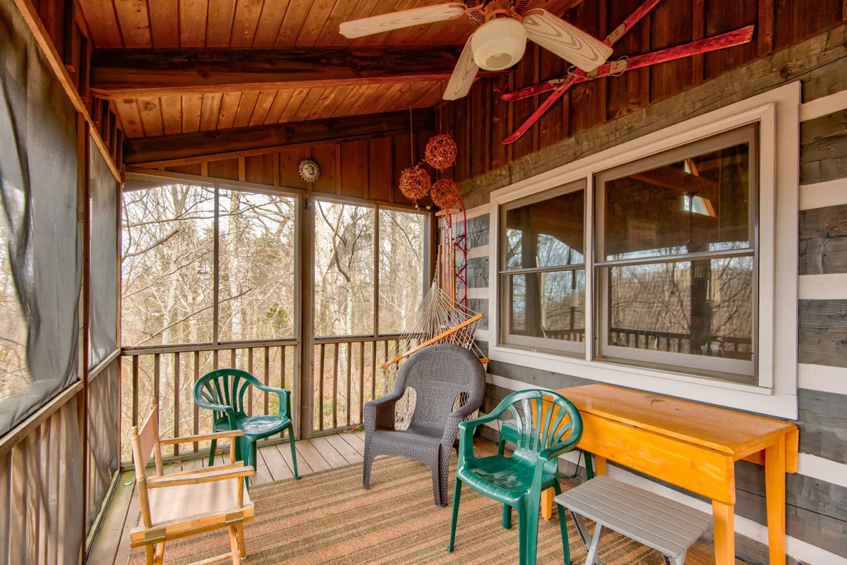 A tranquil screened porch features a hammock, wooden table, and green chairs, with a ceiling fan above. The space is perfectly suited for alfresco dining, board games, or a peaceful nap while remaining sheltered from the elements.
