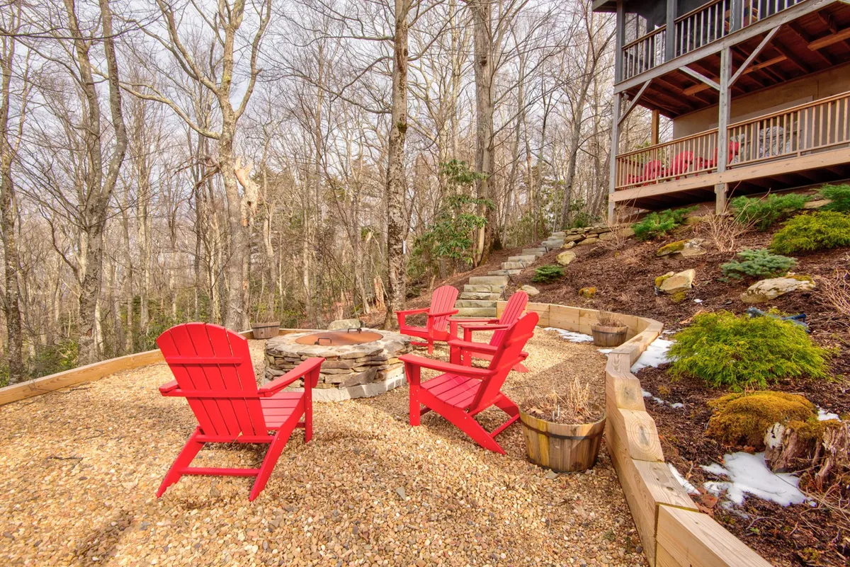 An inviting outdoor fire pit area surrounded by red Adirondack chairs and encircled by trees. The space is designed for socializing, stargazing, and making memories around the warmth of a fire, providing an ideal setting for families and friends to gather under the open sky.