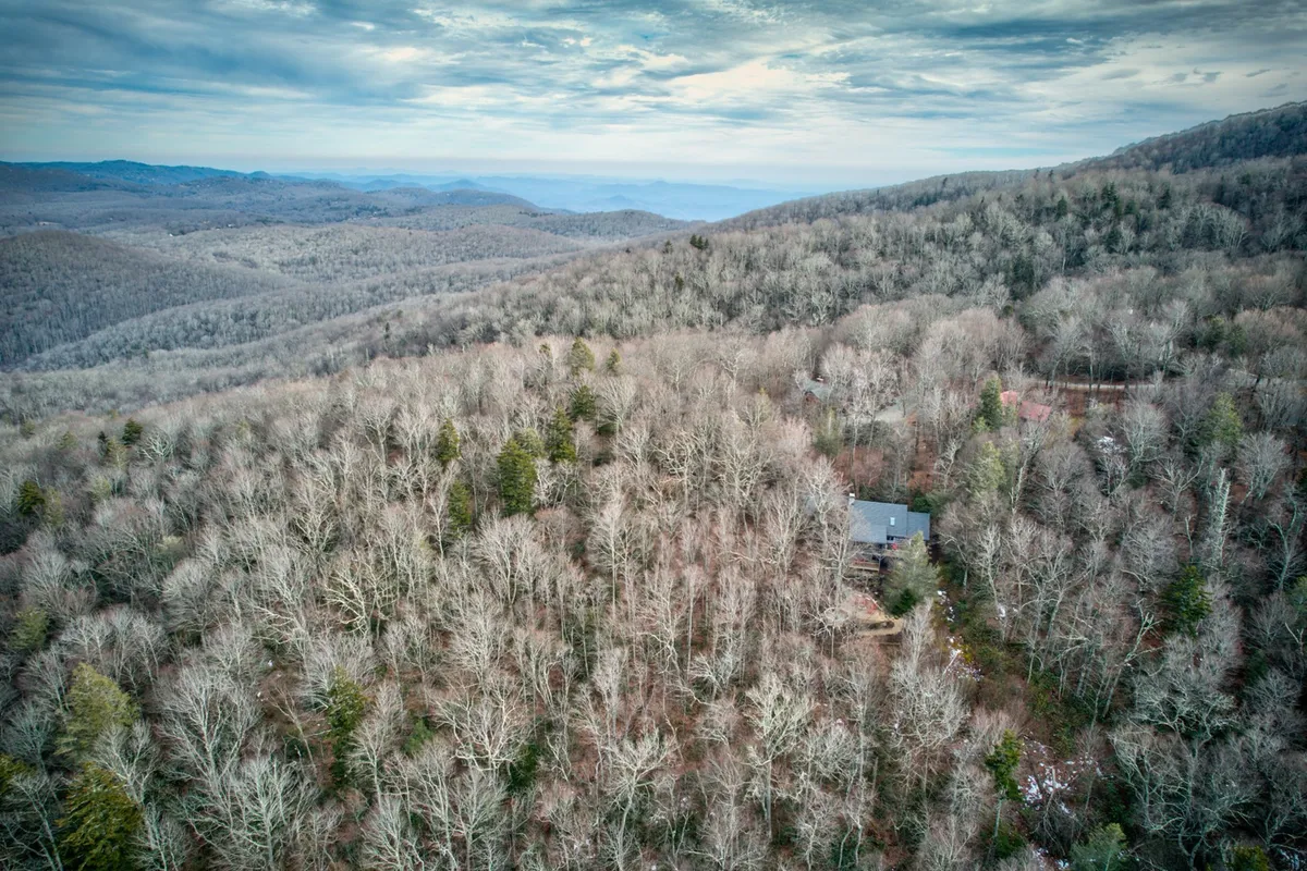 A sweeping vista of rugged mountains and dense forests surrounds a single house, evoking the majesty of the Blue Ridge landscape. The foreground features a tranquil forest, while the distant mountain peaks hint at countless trails and outdoor adventures awaiting exploration. In winter, the scene transforms into a snowy wonderland, perfect for winter sports.