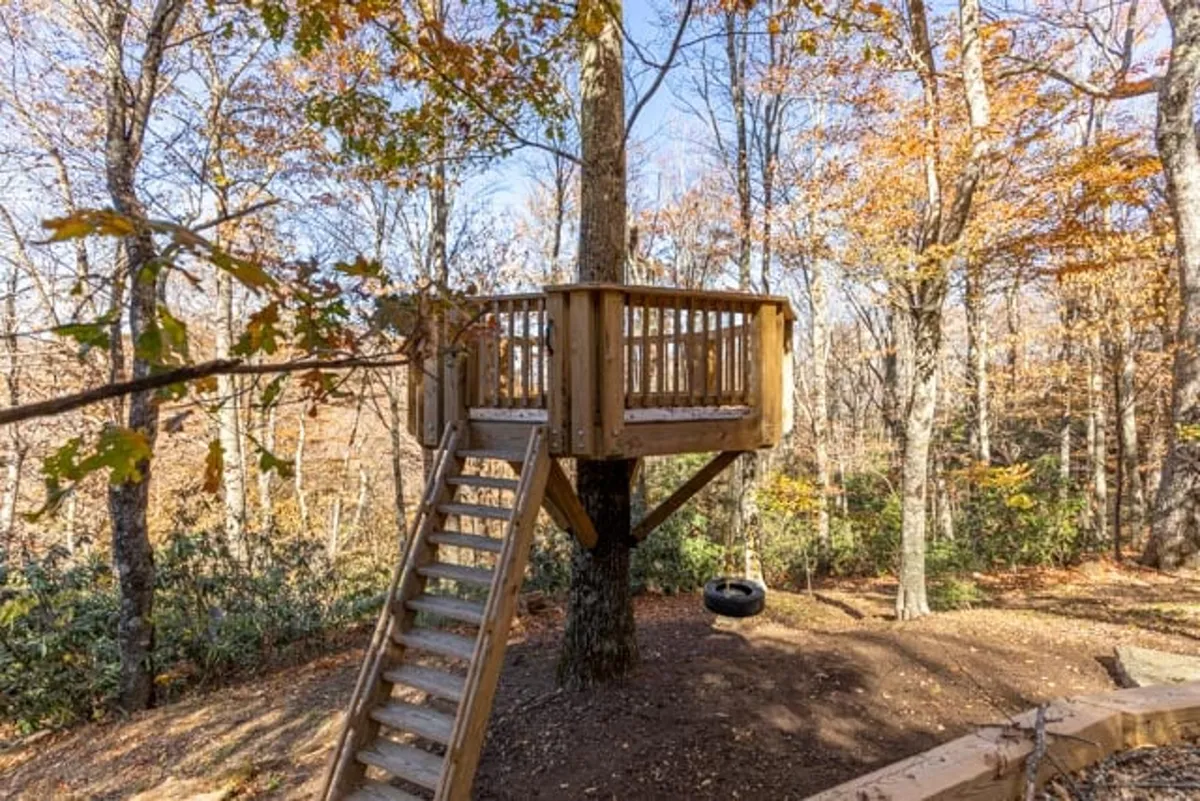 This image features a charming treehouse nestled among towering trees, accessible via wooden stairs. A swing hangs nearby, hinting at imaginative play and outdoor adventures for children. The scene radiates joy and nostalgia, perfectly embodying a playful, family-friendly backyard escape.