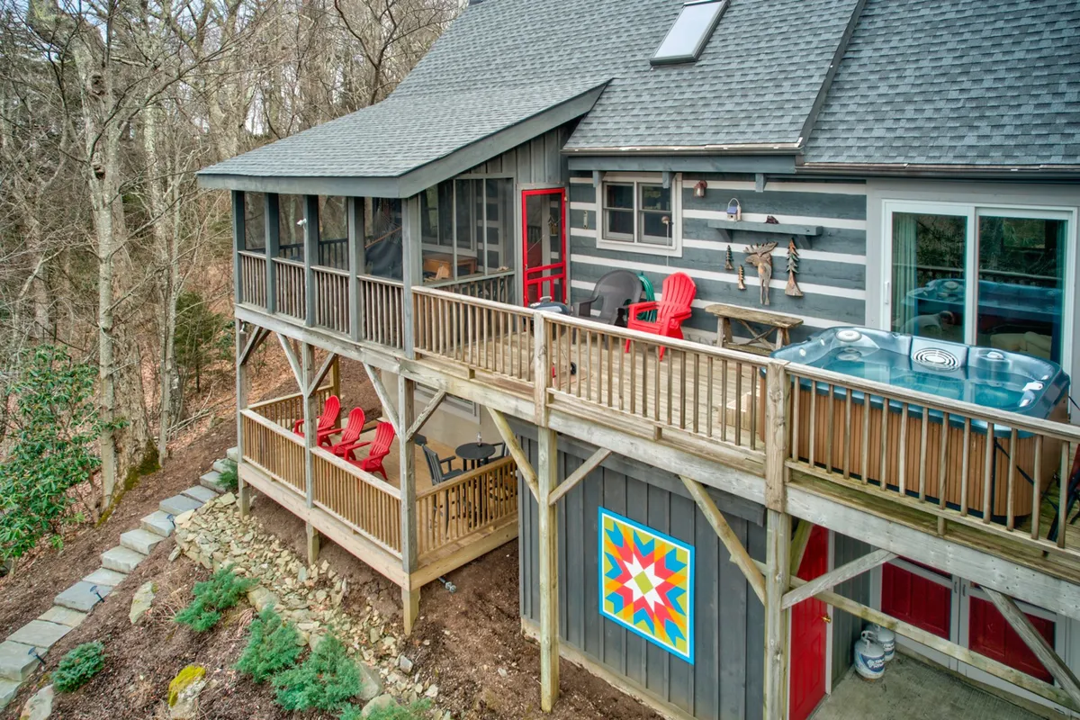 A spacious wooden deck with a bubbling hot tub is complemented by colorful wall art and red chairs. The setting is ideal for socializing, soaking, and enjoying the natural views, with easy access to the interior and year-round scenic vistas.