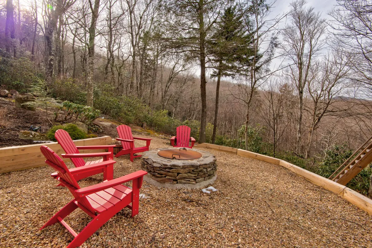 Red Adirondack chairs circle a stone fire pit in a lush, natural backyard setting. The environment conveys a sense of warmth and camaraderie, ideal for evening gatherings and storytelling beneath the stars.
