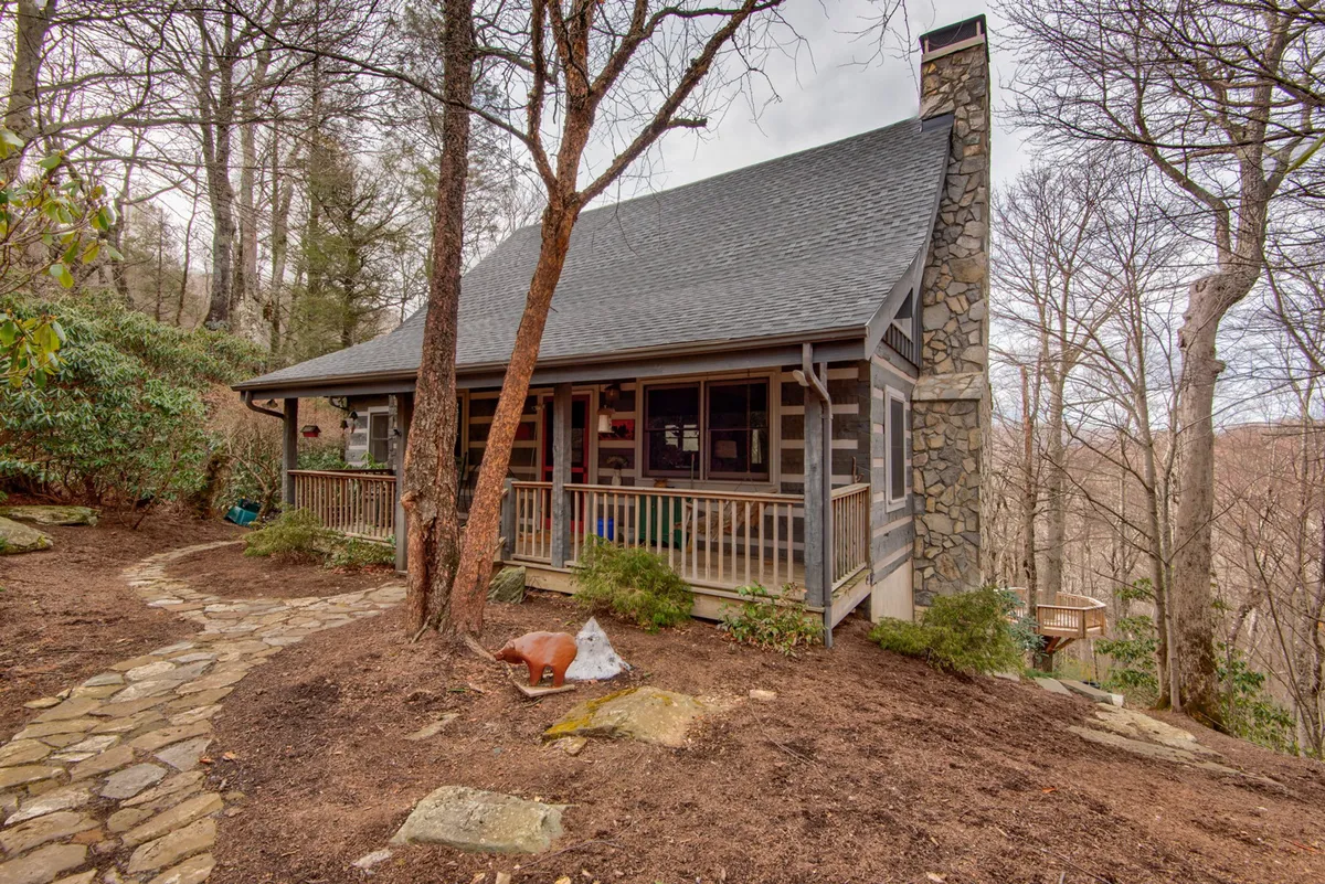 This image captures the exterior of Scarborough Fair, featuring a welcoming wooden porch with decorative figurines, a stone chimney, and a pathway leading through lush greenery. The porch exudes calm and invites guests to relax while enjoying the peaceful natural setting.